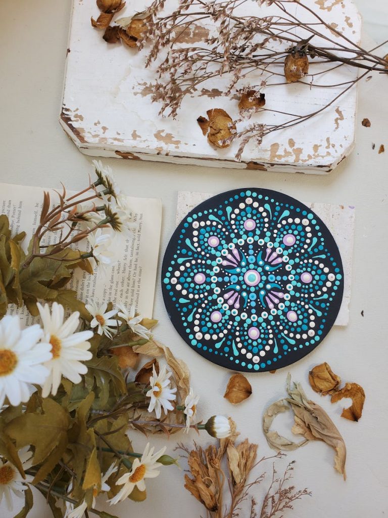 Beautiful handmade mandala art surrounded by dried flowers and daisies.